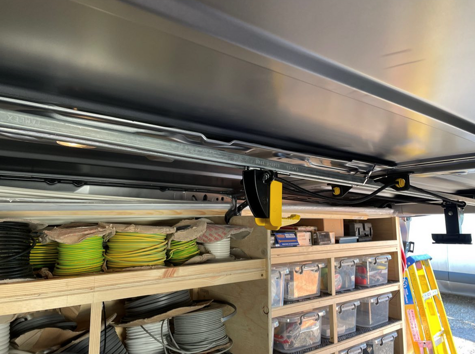 A close-up view of a JET Rack mounted above wooden storage shelves inside a vehicle or workshop. The mechanism includes metal rails, black and yellow components, and a large silver garage door panel.